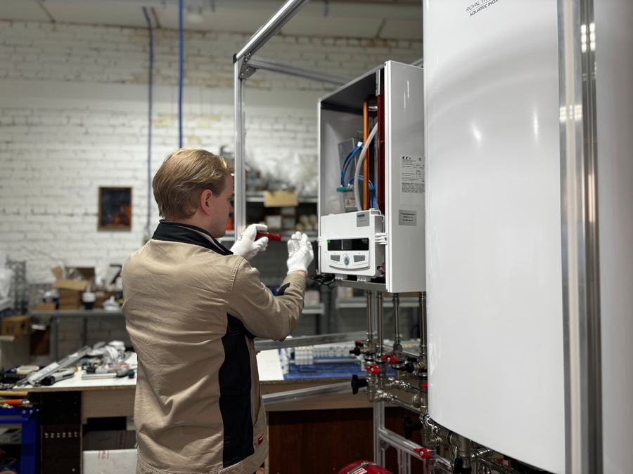 Technicien en veste beige contrôlant le tableau de commande d'une chaudière murale