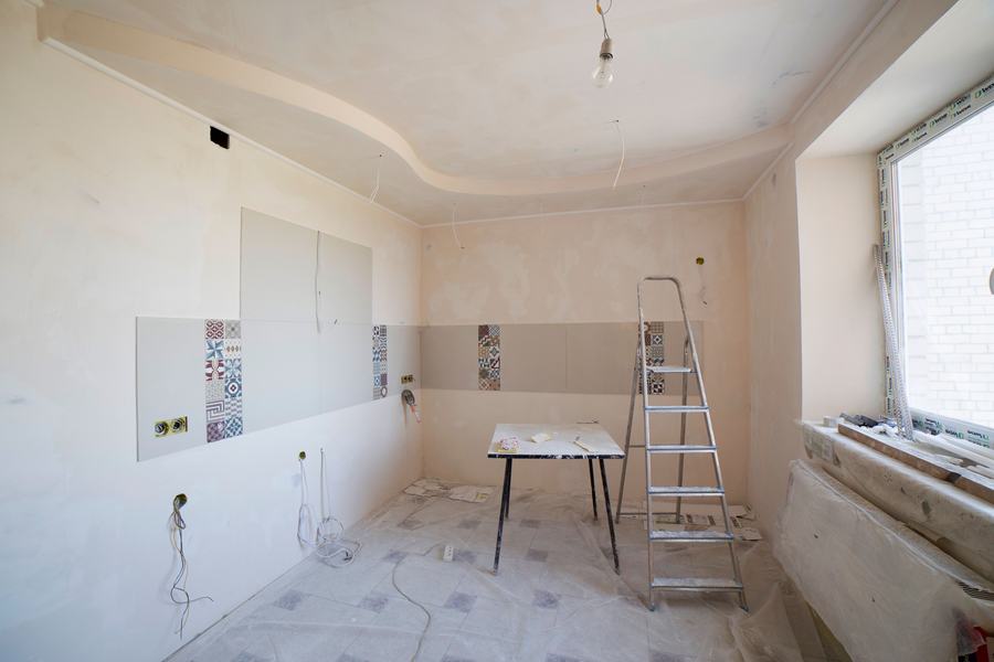 Cuisine en cours de rénovation avec une échelle, des murs enduits et du carrelage posé en échantillon
