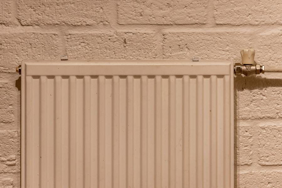 Radiateur blanc à éléments fixé sur un mur de brique enduit